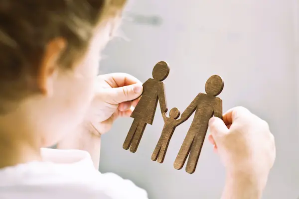 Niña sostiene figuras de padres e hijo, reflejando disputa legal por custodia compartida cuando la madre se opone.