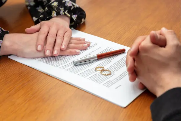 Pareja frente a documento con anillos y bolígrafo, representando el trámite legal de un divorcio notarial.