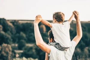 Niño sentado en los hombros de su padre en un campo, vinculado a dudas sobre visitas y custodia tras separación.