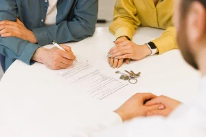 Pareja firma documentos con llaves sobre la mesa, representando acuerdos de alquiler tras una separación.
