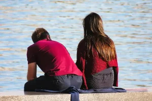 Pareja sentada frente al agua en actitud distante, simbolizando el proceso emocional y legal de cancelar una pareja de hecho.