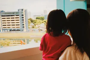 Madre e hija observan la ciudad desde un balcón, ilustrando el concepto de casa nido en la custodia compartida.