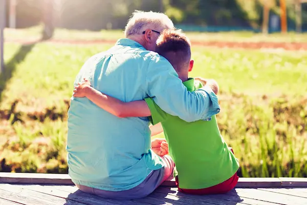 Abuelo abraza con ternura a su nieto mientras se sientan al aire libre, representando los derechos de los abuelos.