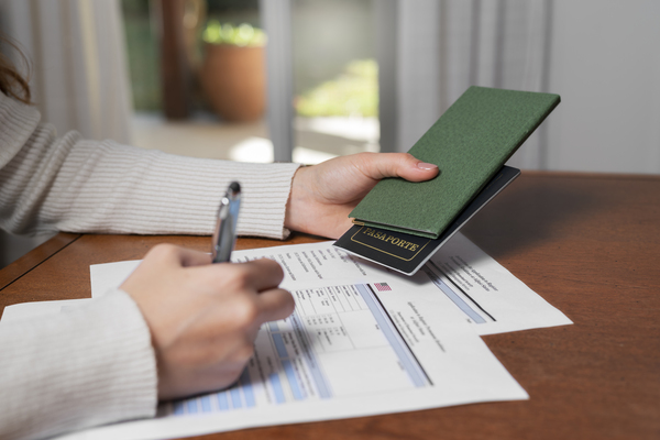Persona rellenando formularios mientras sostiene un pasaporte, en proceso de solicitar la residencia temporal en España.